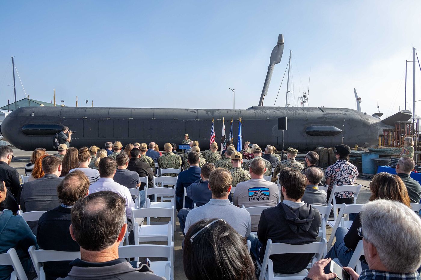 An audience seated outdoors in front of a very large uncrewed undersea vehicle